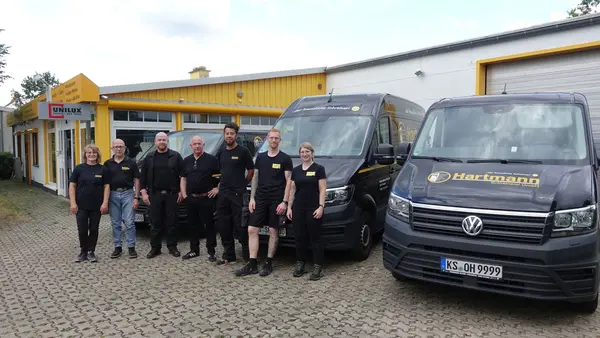 Das Team der Schreinerei Hartmann steht vor dem Firmengebäude und Firmenfahrzeugen.