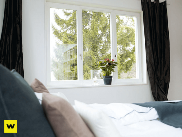 Helles Schlafzimmer mit großem Fenster, Vorhängen und Zimmerpflanze auf der Fensterbank.
