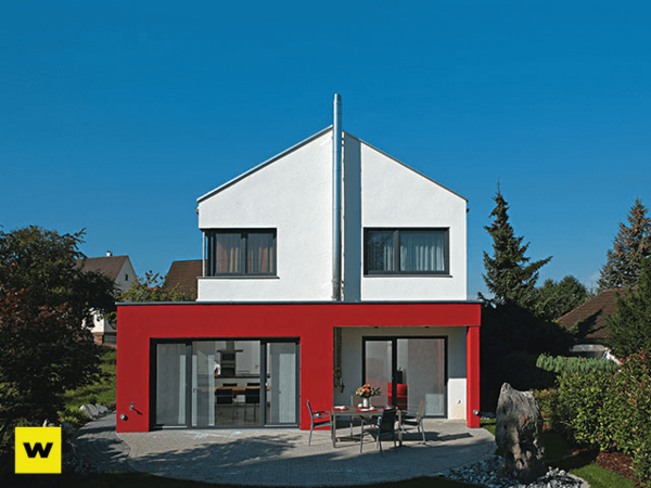 Modernes Einfamilienhaus mit roter Fassade, Terrasse und Garten bei blauem Himmel.