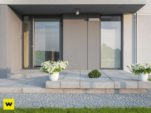 Moderner Hauseingang mit großen Glasflächen, grauen Fliesen und weißen Blumenkübeln.