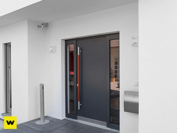 Moderne, graue Haustür mit Seitenteil und Edelstahlgriff an weißer Hausfassade.
